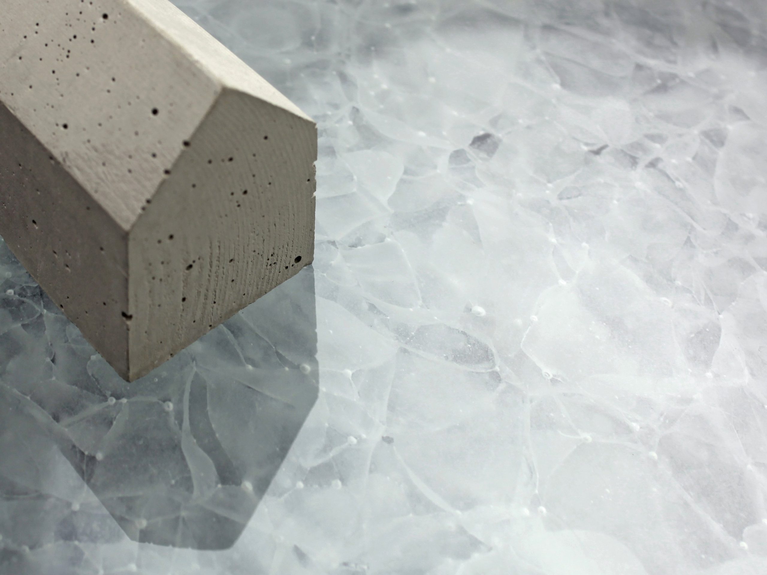 FutureStone Glaslaminat-Platte mit Eis-Kristallstruktur in Hellblau neben grauem Betonwuerfel als Materialvergleich