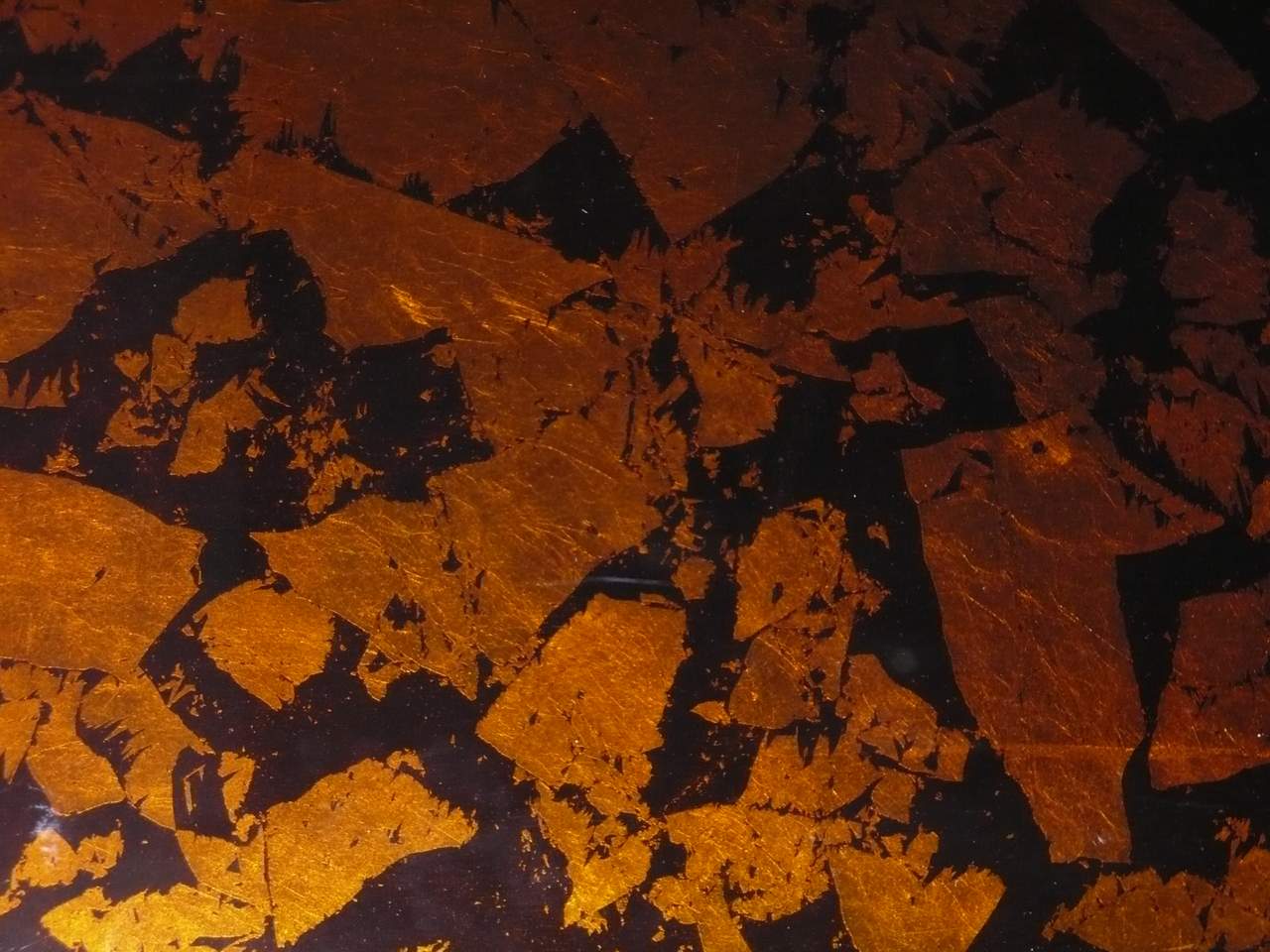 Glaslaminat-Detail mit einlaminierter Kupferfolie in bernsteinfarbenen und braunen Toenen auf schwarzem Grund