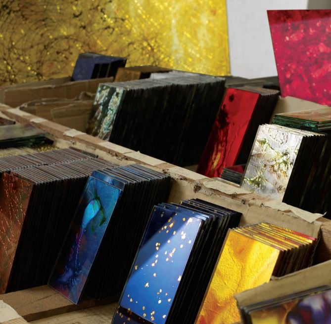 Regale mit zahlreichen bunten Glaslaminat-Mustern in Gold, Blau, Rot, Silber und weiteren Farben aufgereiht