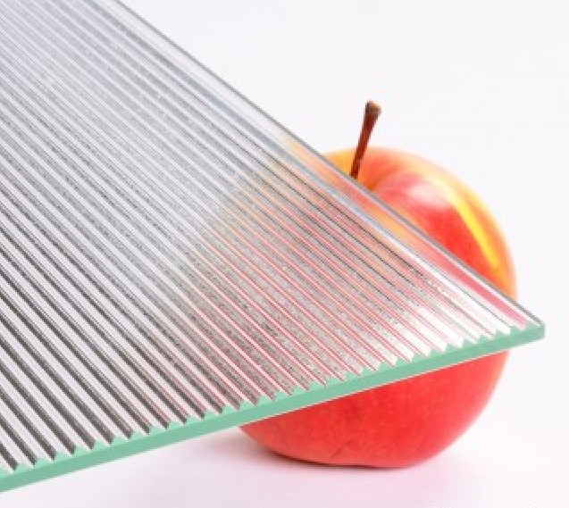 Transparentes Reliefglas mit feinen parallelen Rillen als Linienmuster, dahinter ein Apfel als Groessenreferenz