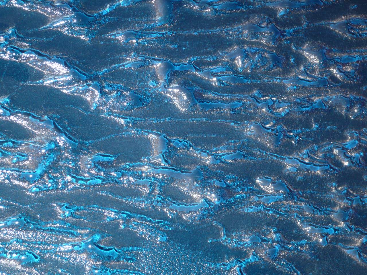 Nahaufnahme einer blauen Schmelzglas-Oberflaeche mit fliessender Wellenstruktur und Lichtreflexionen