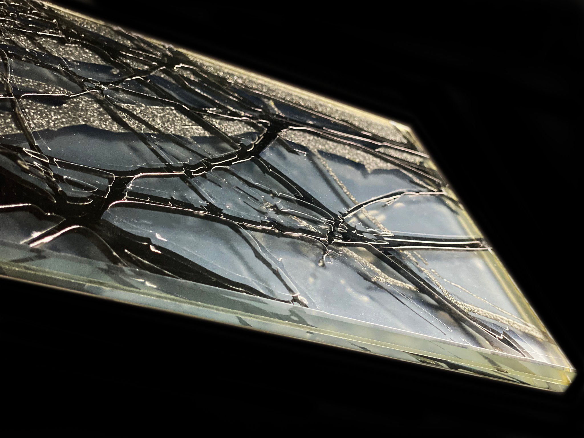 Schmelzglas-Platte mit Craquele-Bruchstruktur in transparenten und goldenen Toenen auf schwarzem Hintergrund