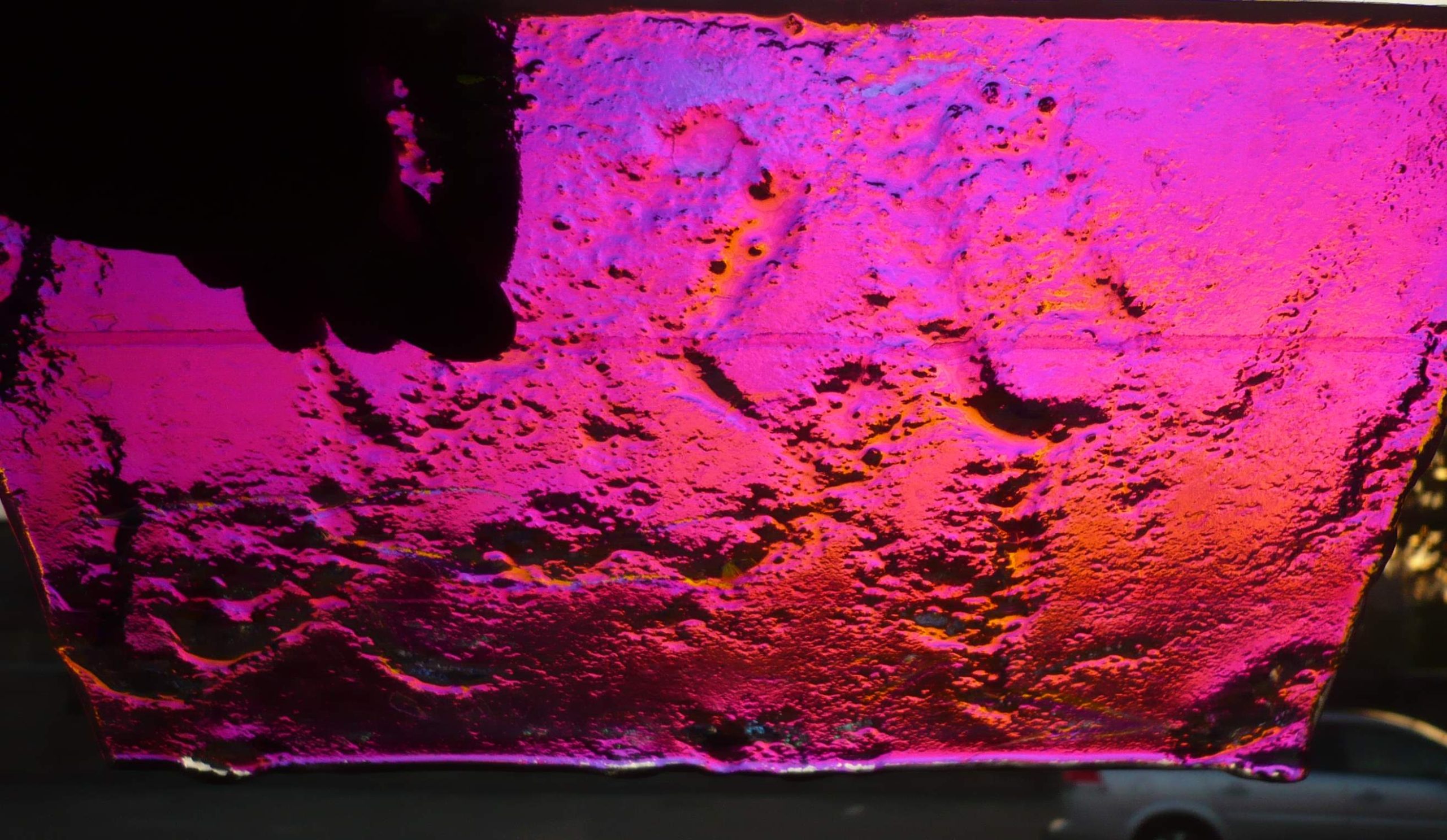 Dichroitisches Schmelzglas-Stueck in leuchtendem Pink-Magenta mit strukturierter Oberflaeche und LED-Beleuchtung