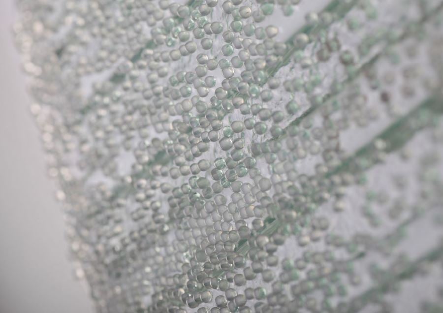 Nahaufnahme eines Schmelzglases mit eingeschmolzenen kleinen Glasperlen in diagonalem Zickzack-Muster