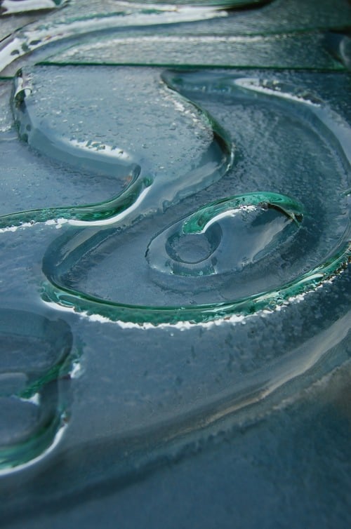 Nahaufnahme eines tuerkisfarbenen Schmelzglases mit spiralfoermigem Relief und organischen Wellenmustern
